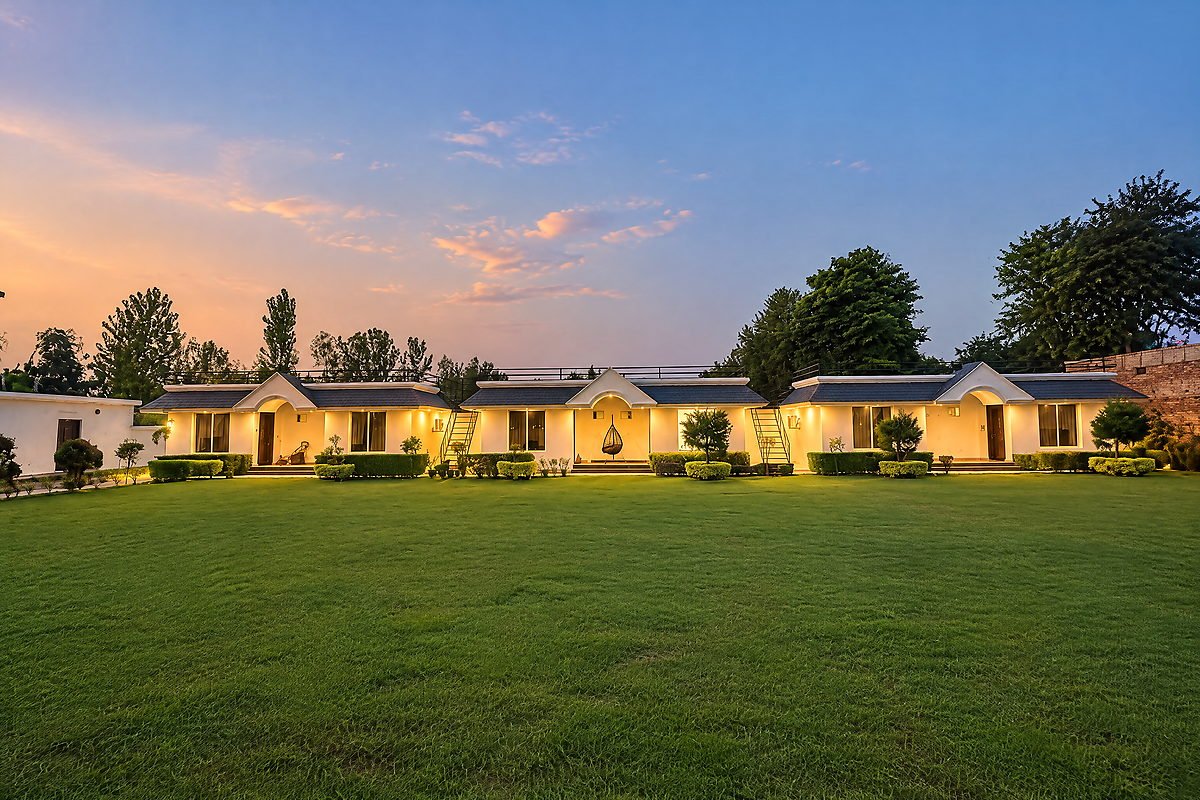 The event lawn with warmly illuminated cottages behind it at The White House Pilibhit