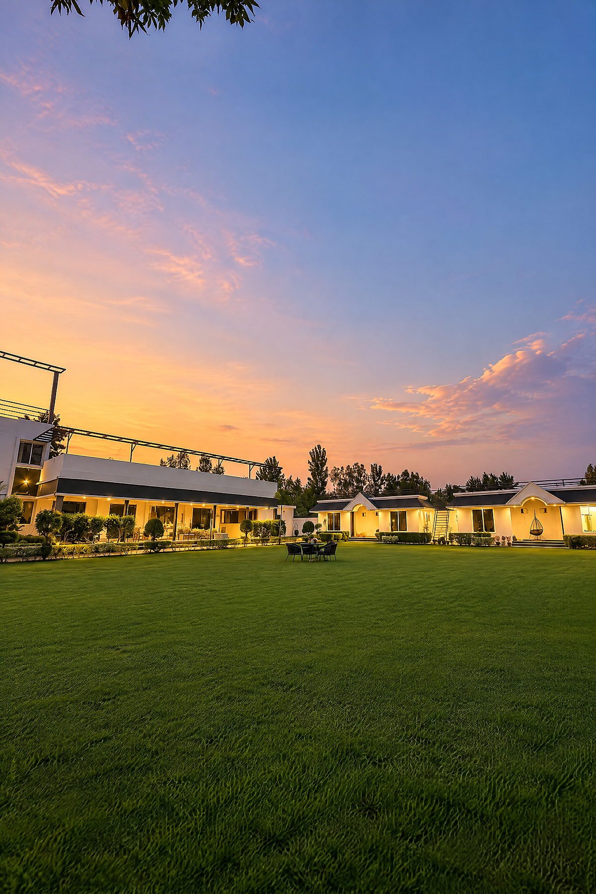 Sunset over the lawn and illuminated cottages at The White House Pilibhit